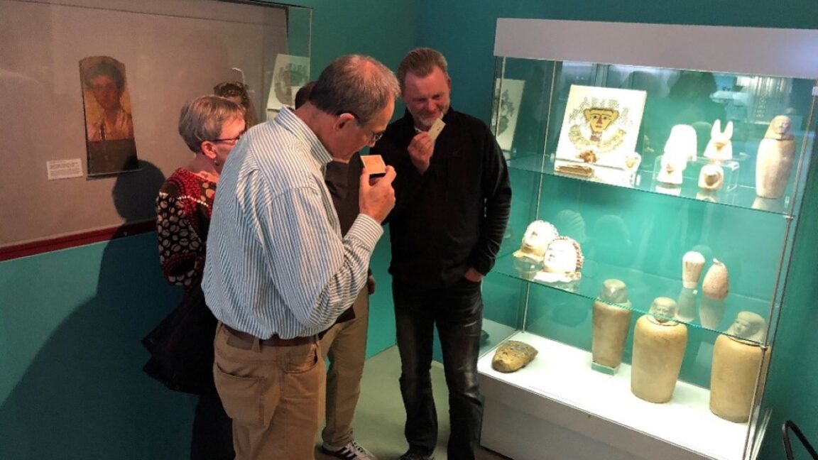 Museum visitor examining ancient Egyptian canopic jar with scented display card nearby