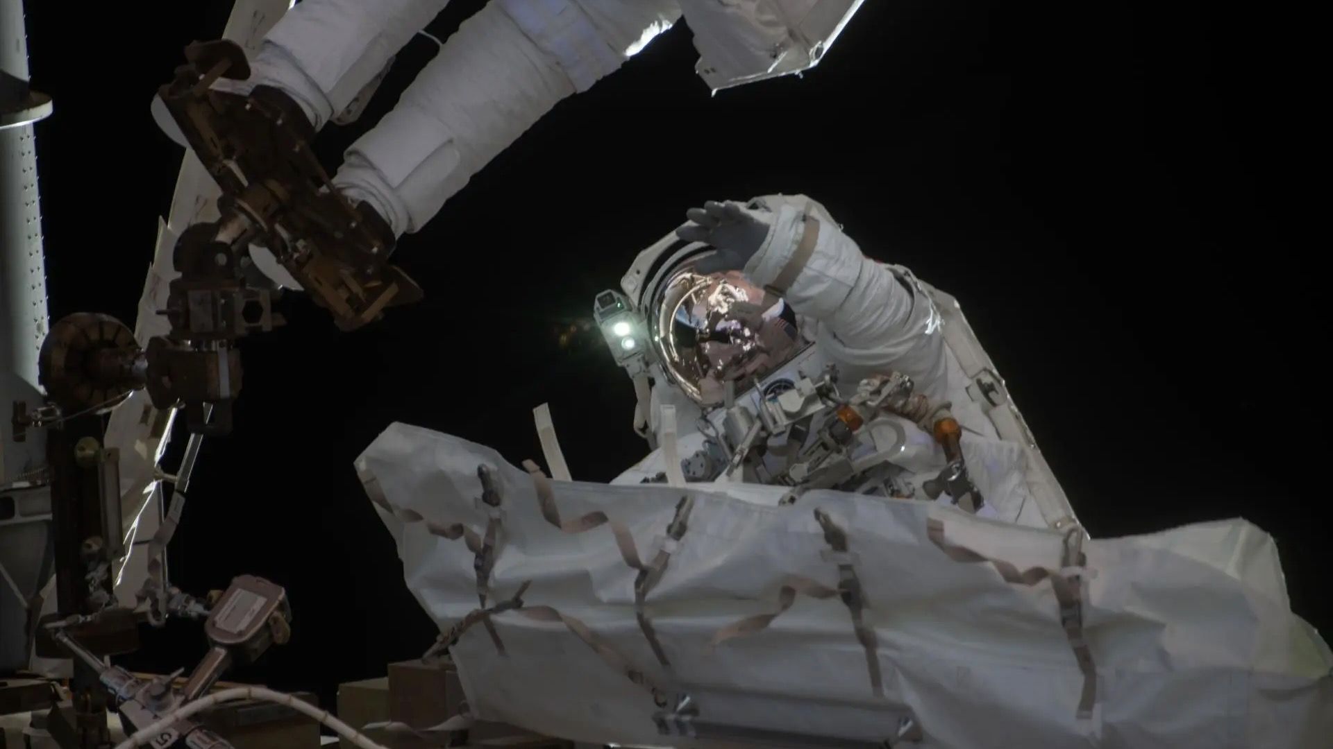 NASA astronaut in white spacesuit waves at camera during spacewalk outside International Space Station