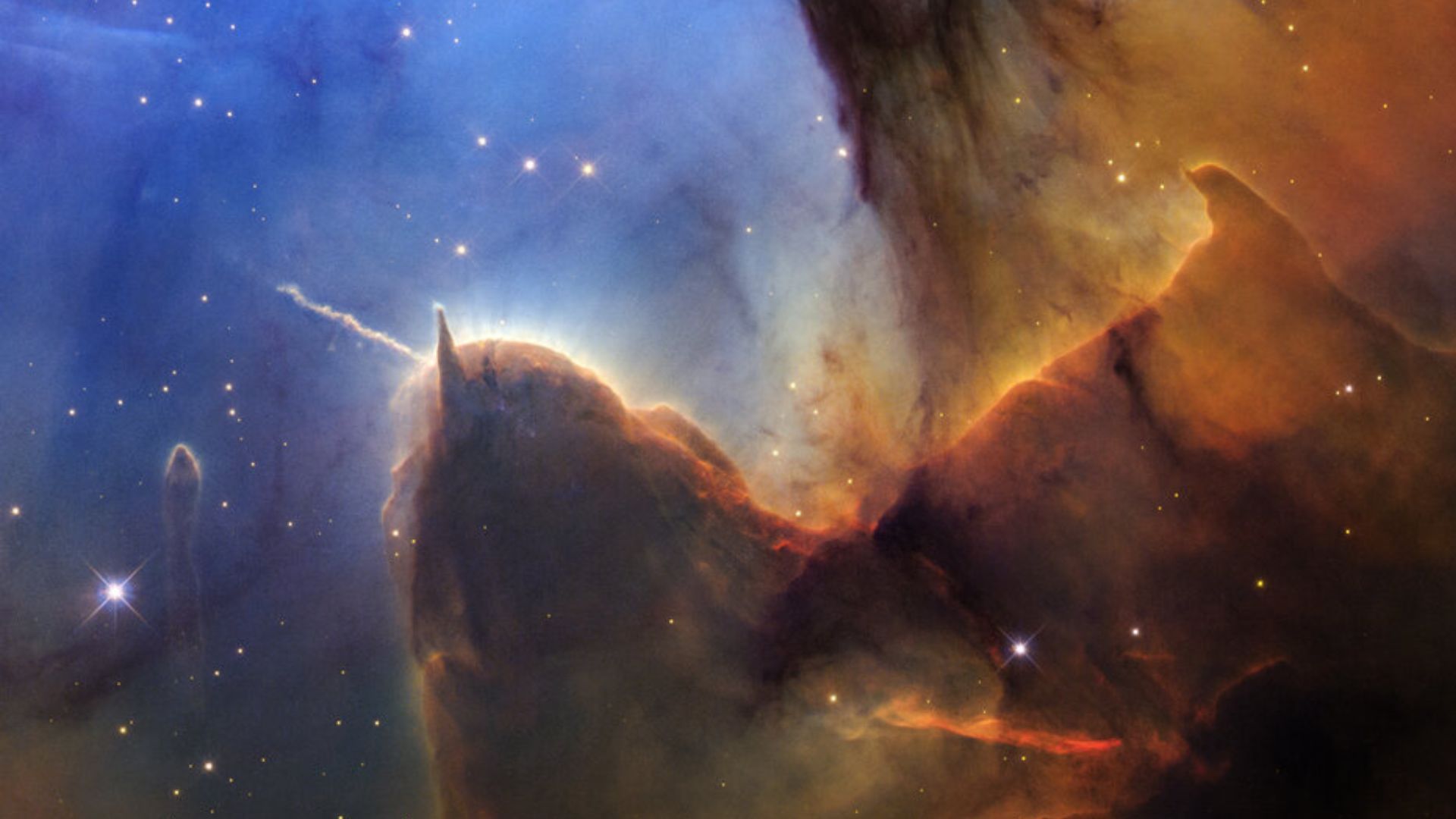 Colorful Trifid Nebula showing orange glowing gas clouds, blue cleared regions, and dark dust captured by Hubble telescope