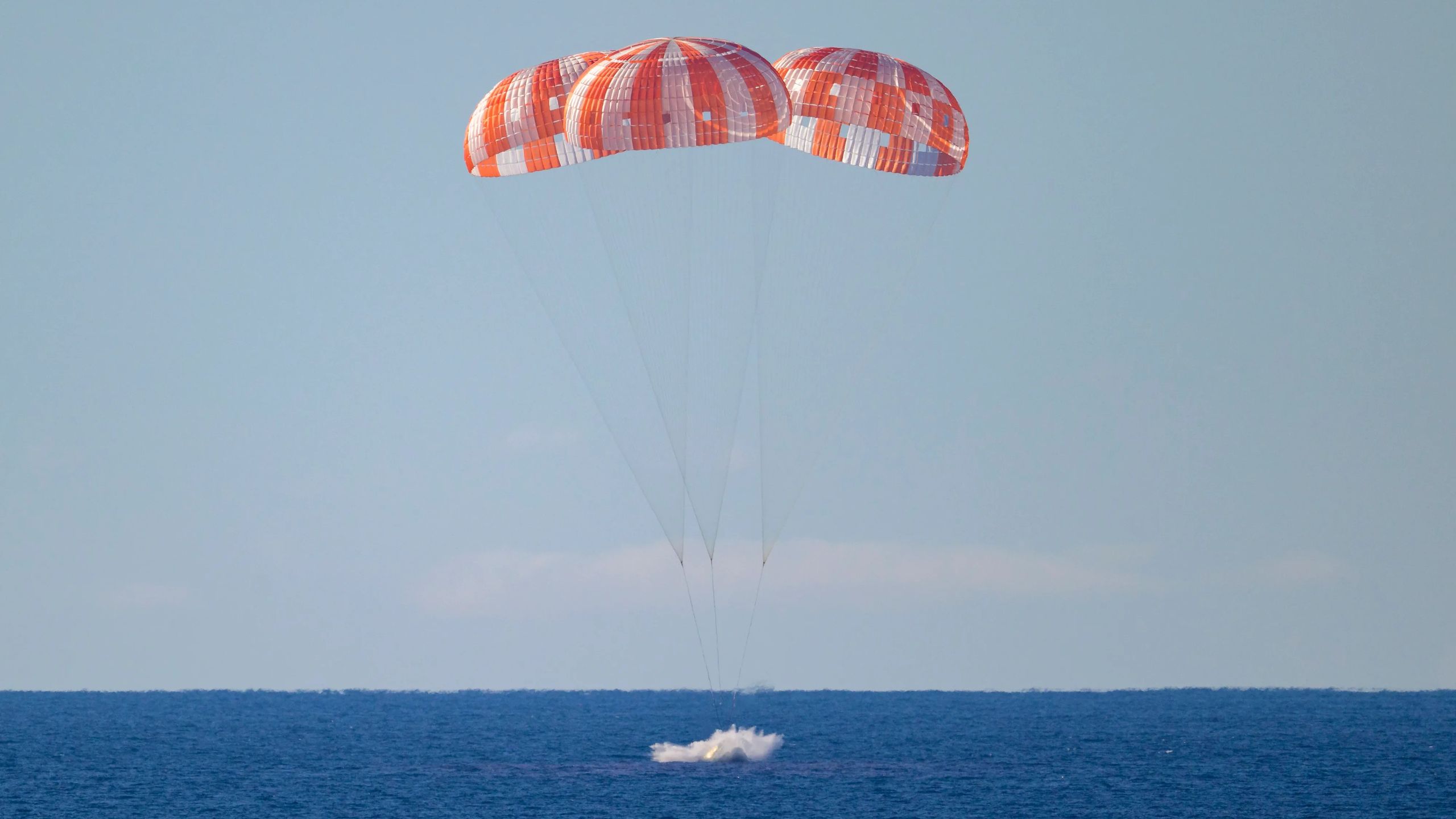NASA Orion spacecraft floating in Pacific Ocean with recovery parachutes deployed overhead