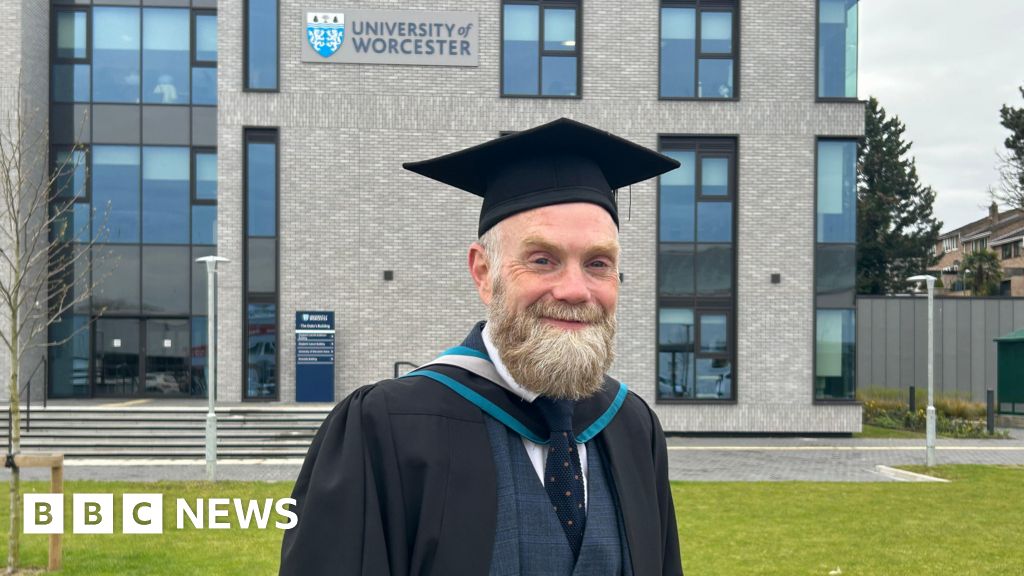 Chris Garratt holding graduation gown and mortarboard cap while wearing athletic trainers for marathon training