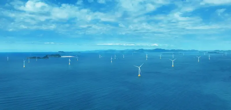 Twenty-five large white offshore wind turbines standing in ocean waters near Kitakyushu, Japan