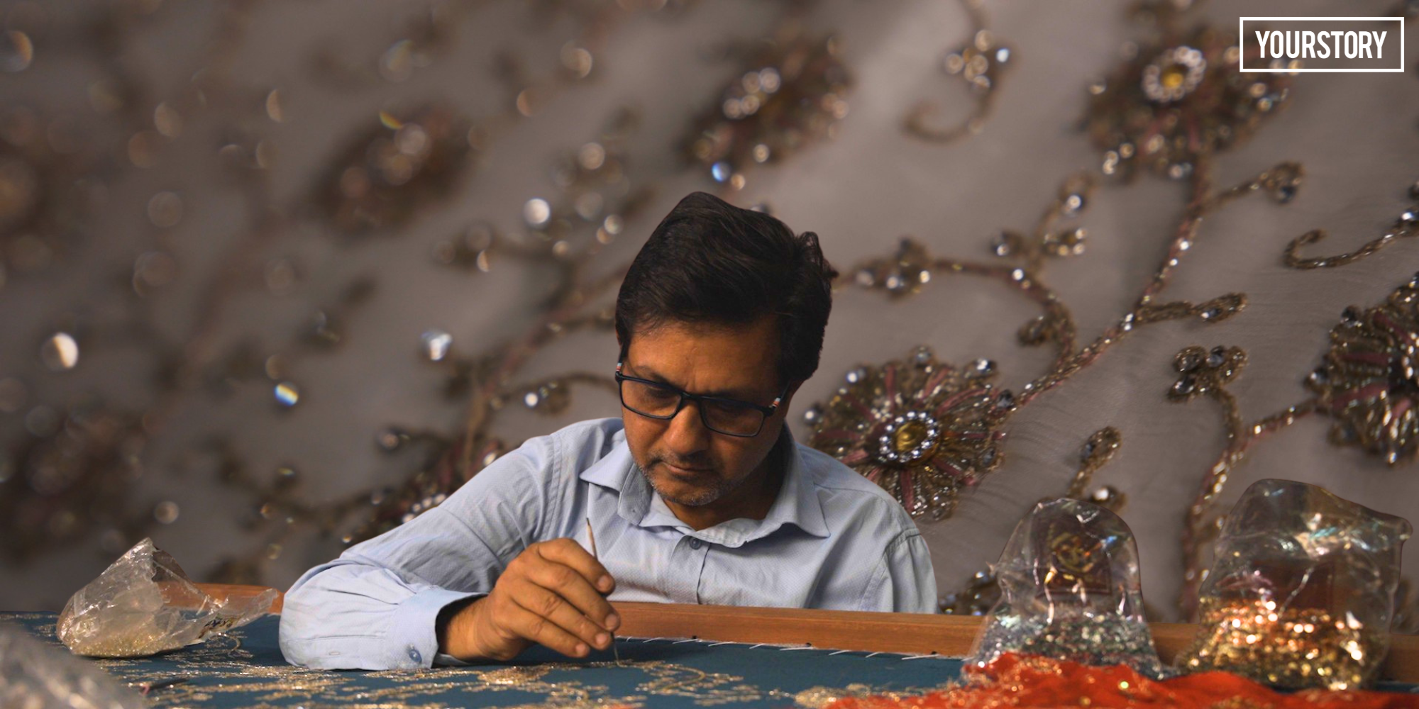 Indian artisan stitching golden zari thread onto fabric stretched on traditional wooden frame