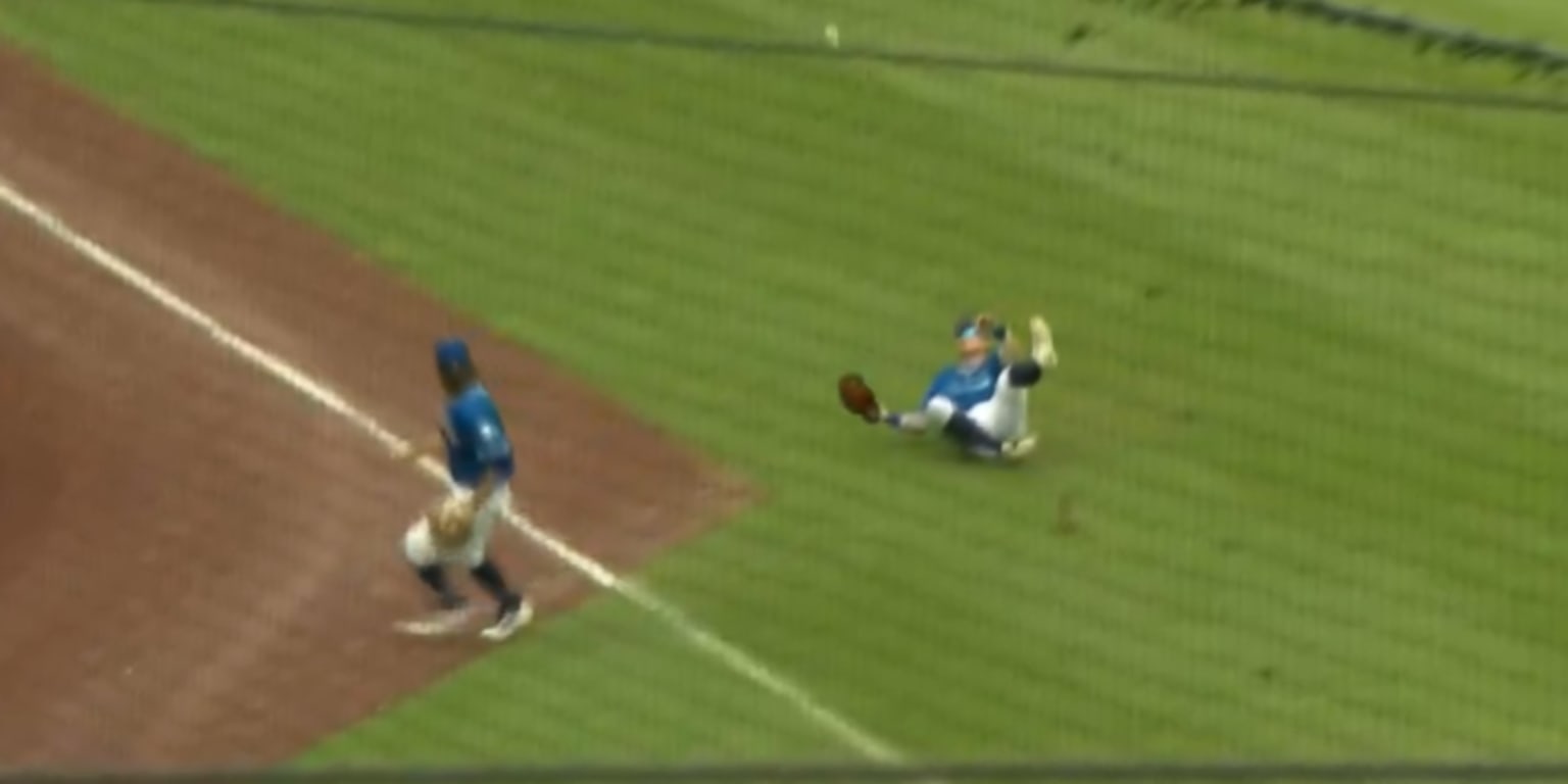Baseball infielder making catch in shallow outfield while teammate slides nearby