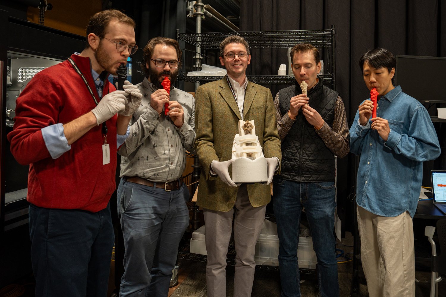 Researchers examining ancient Paracas whistle alongside modern 3D-printed replicas on table
