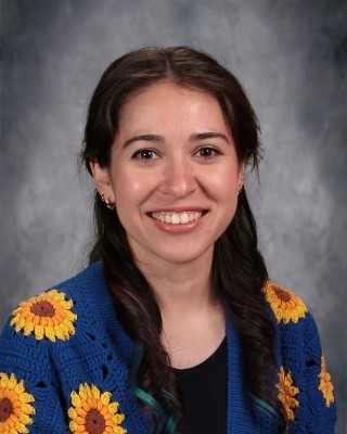Elementary art teacher Noelia Martinez-Voigt smiling with students in her colorful classroom