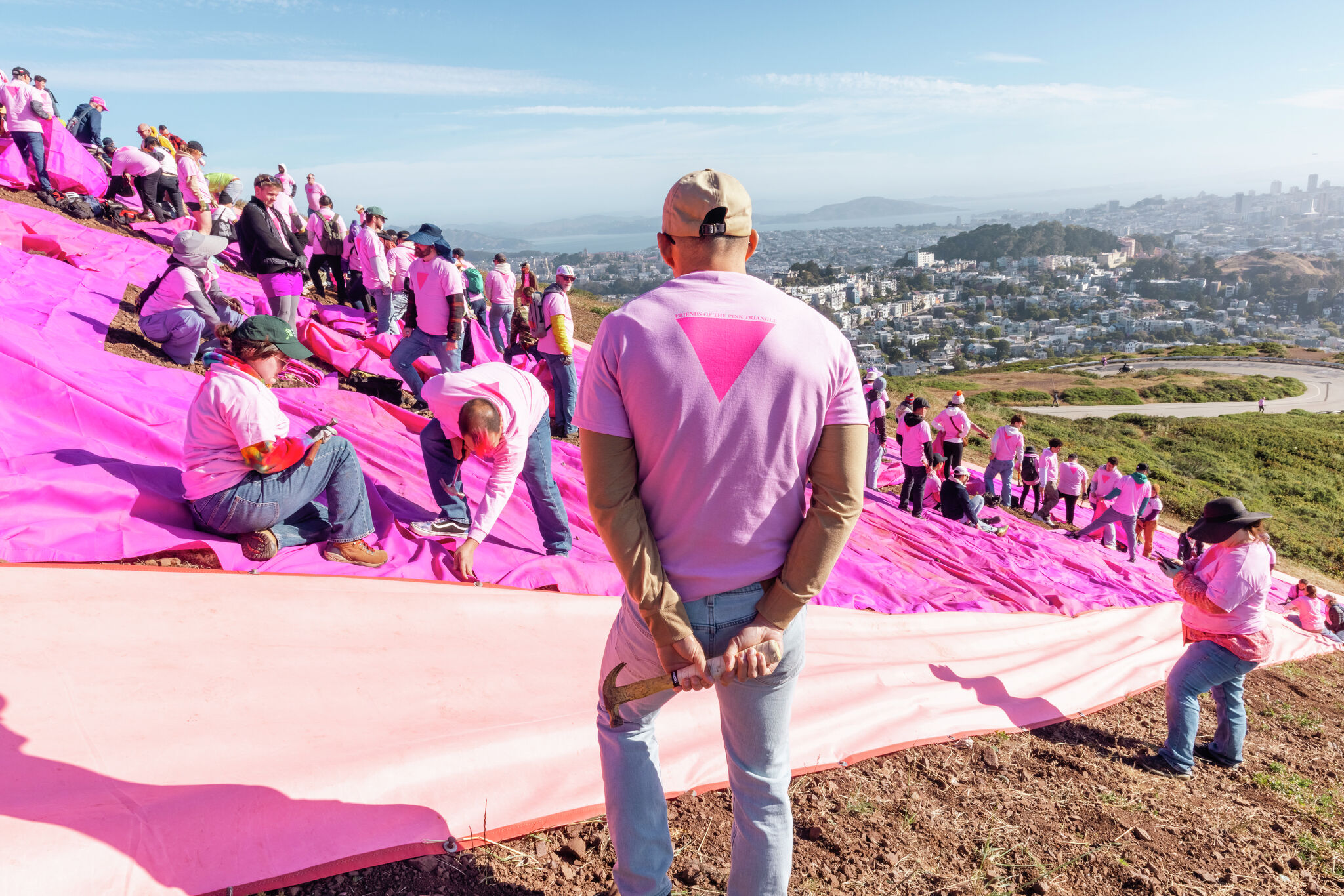 Volunteers in pink shirts hammer stakes on hillside creating massive pink triangle symbol