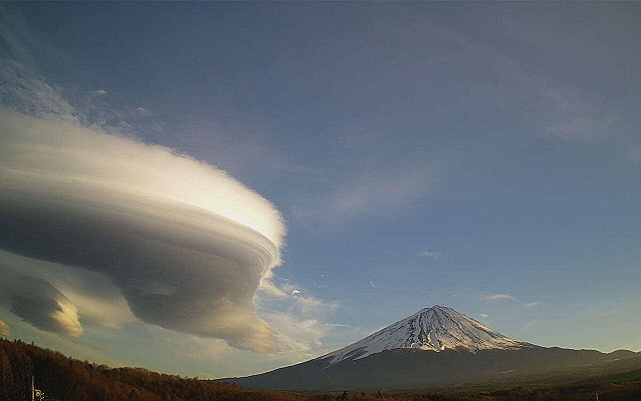 Distinctive cap cloud formation draping over snow-capped Mount Fuji summit against blue sky