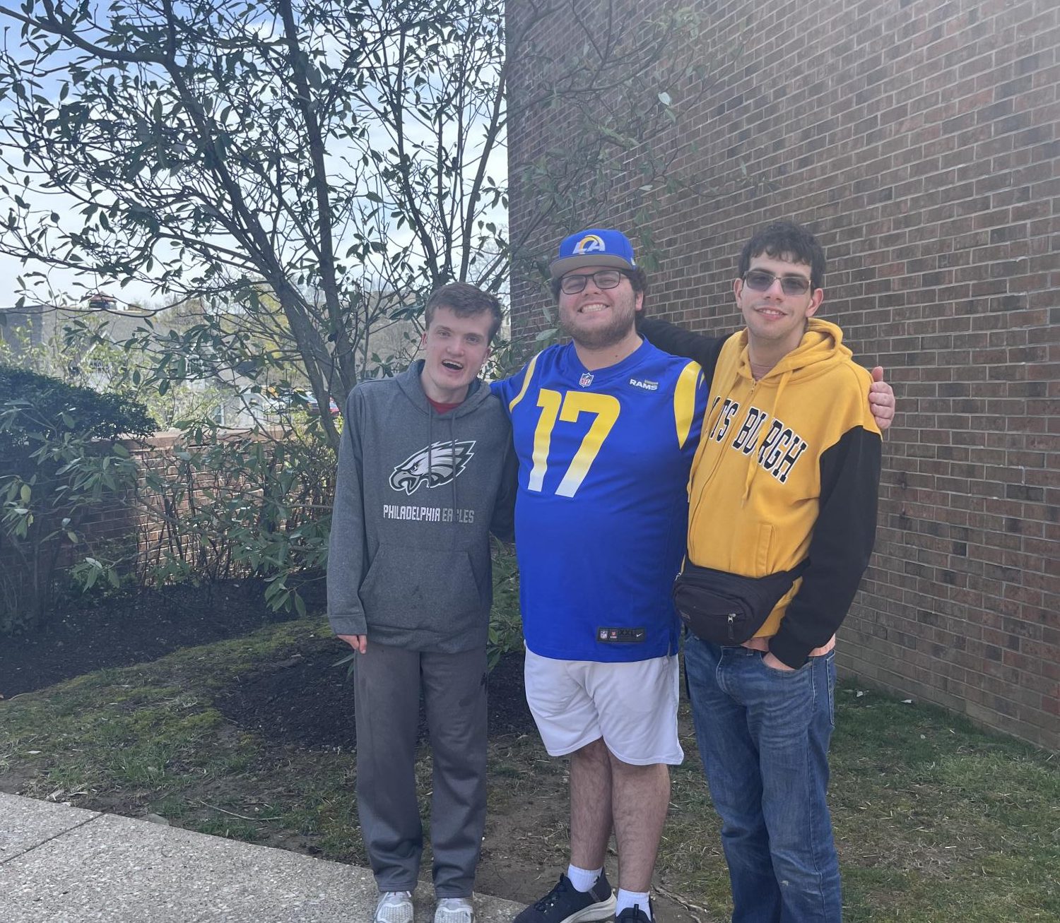 Three smiling male students standing together outdoors on college campus in professional photo