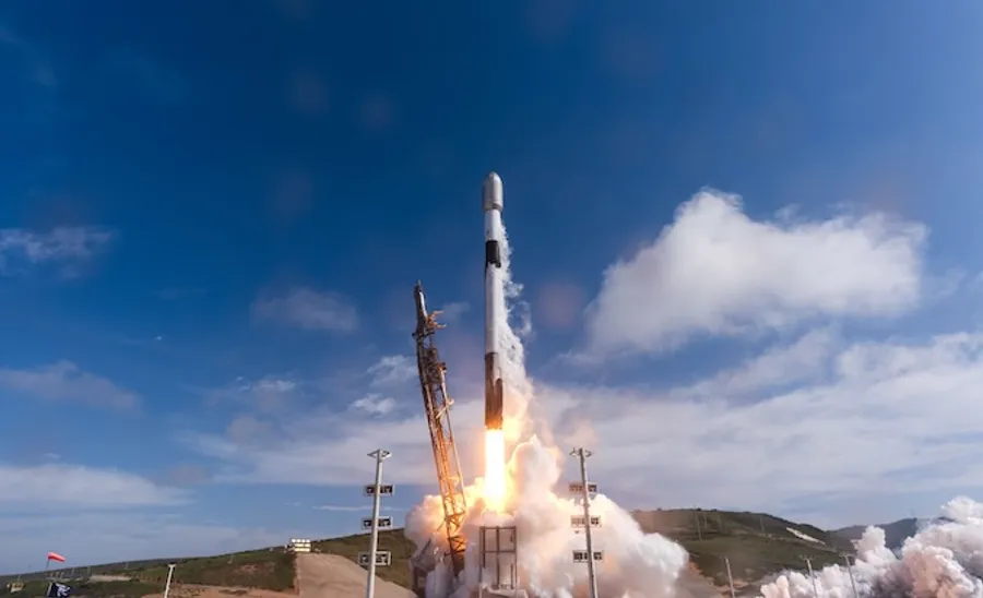 ** SpaceX Falcon 9 rocket launches into blue sky trailing white exhaust plume from California launch pad