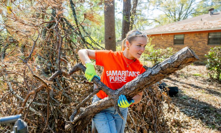 Young volunteers in orange shirts clearing fallen tree branches from residential yard after ice storm