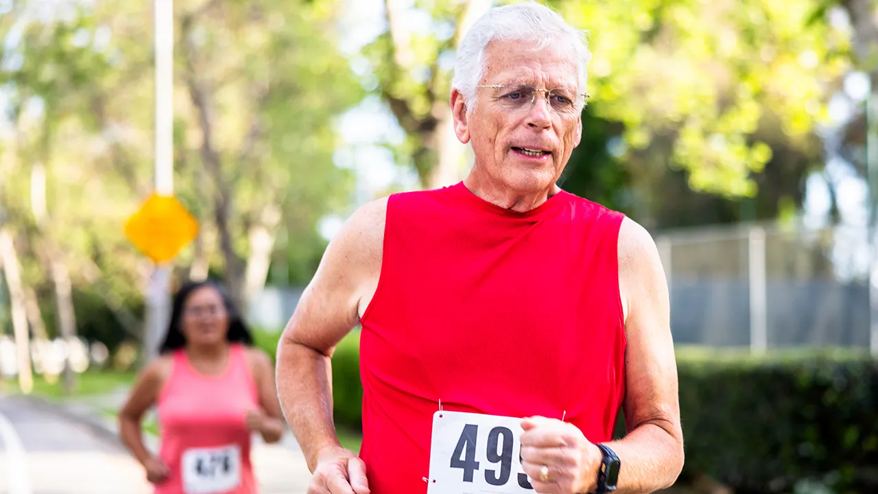 Older male runner in athletic gear checking fitness watch during outdoor exercise