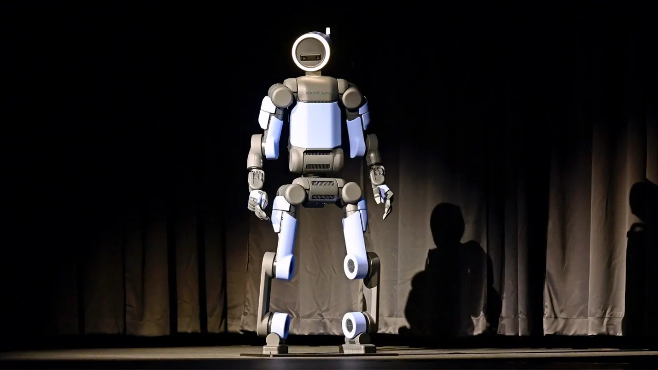 Boston Dynamics Atlas humanoid robot carrying heavy object in manufacturing facility alongside workers