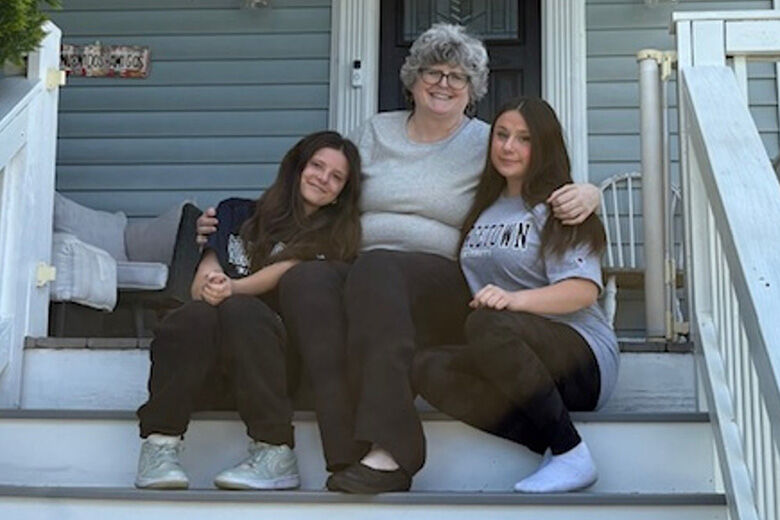 Mary Hylton smiling with her two teenage daughters Claire and Makiah outdoors