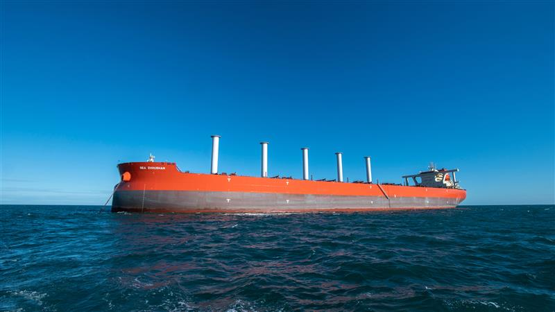 Large ocean-going cargo vessel with modern rotor sails sailing across blue waters