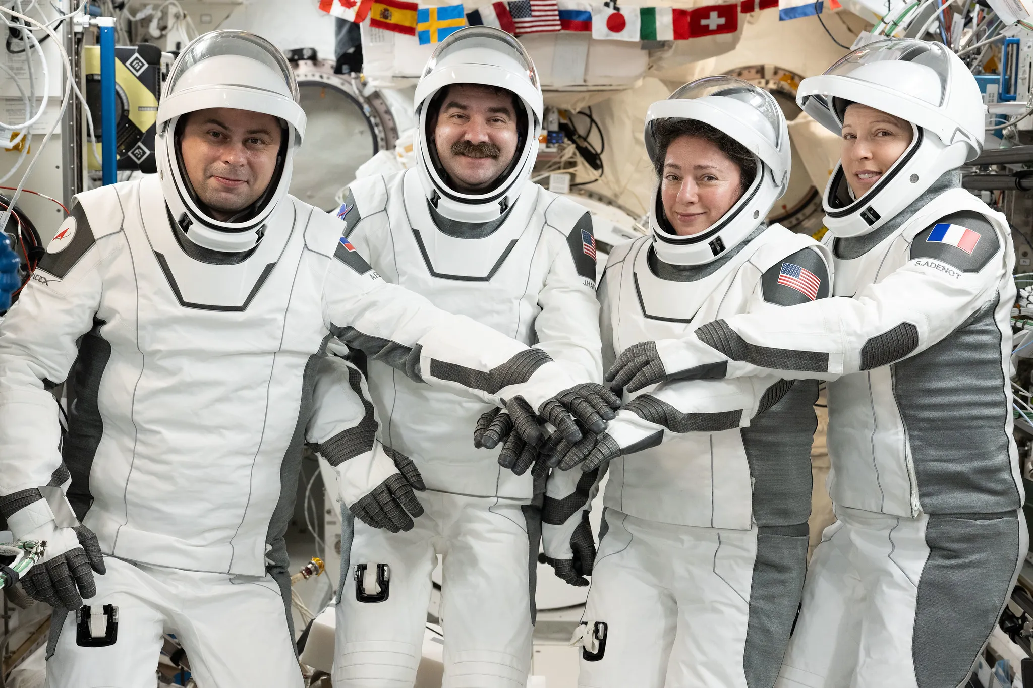 Four Crew-12 astronauts in white SpaceX pressure suits posing together before their space station mission