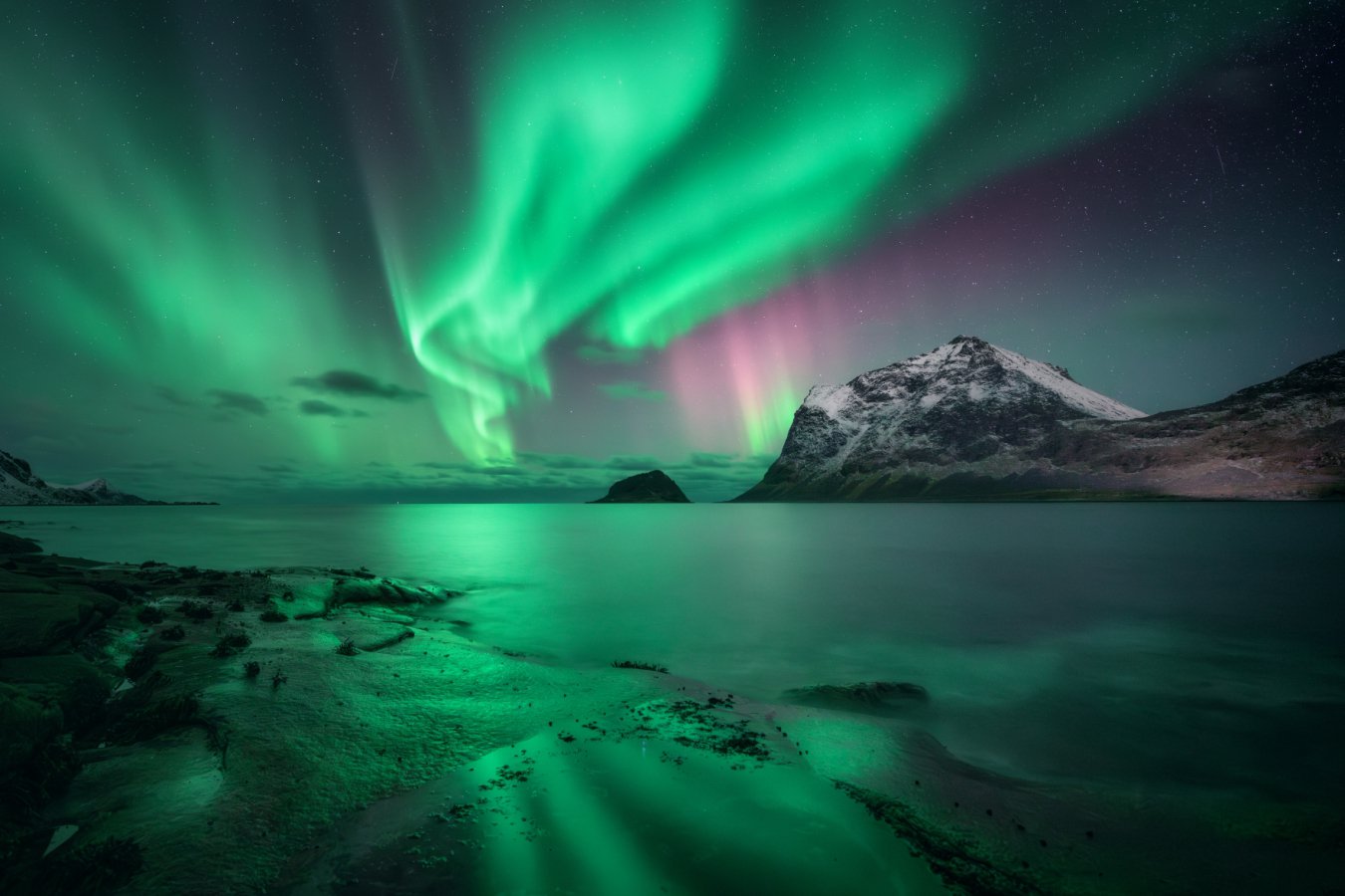 Aurora borealis dancing over snow-covered mountains in Norway's Lofoten islands at night