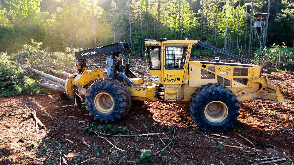 Remote-controlled forestry skidder machine with robotic grapple moving logs in southeastern forest
