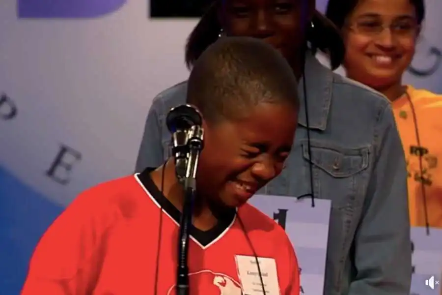 Young boy laughing at microphone during national spelling bee competition on stage