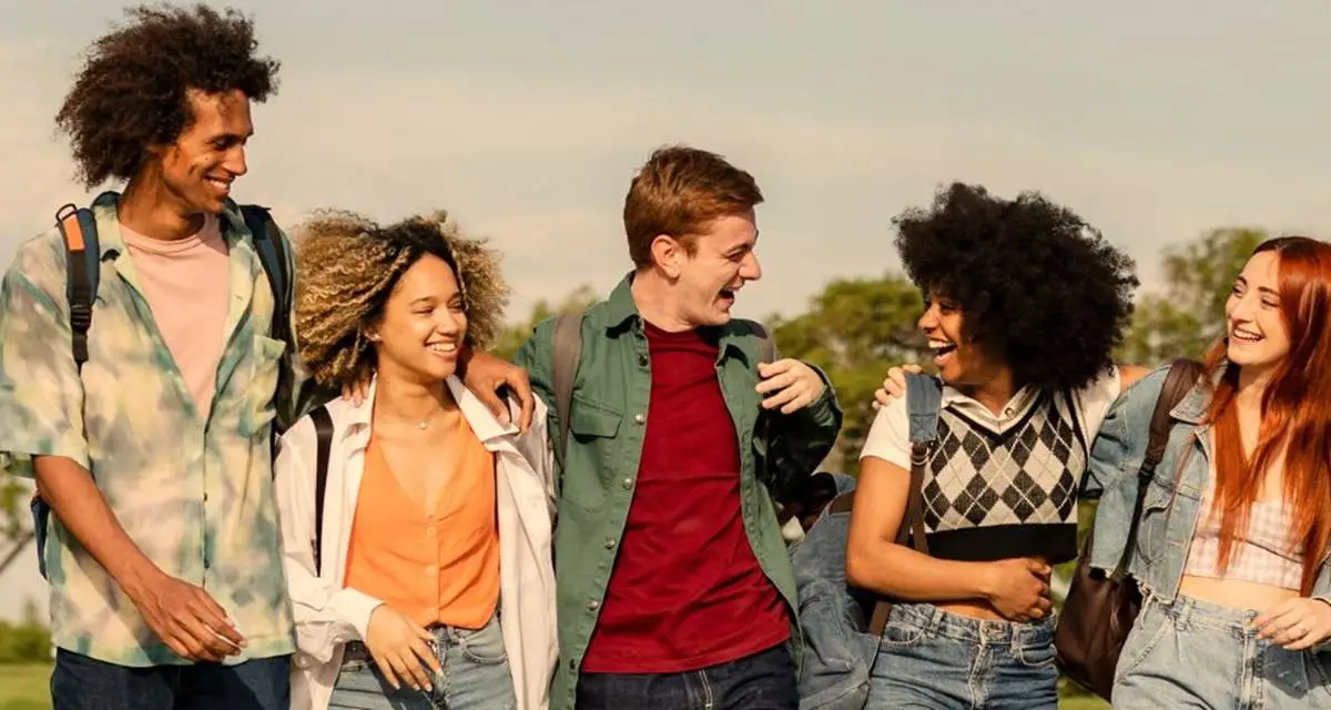 Diverse group of teenagers walking together outdoors on sunny day, smiling and talking