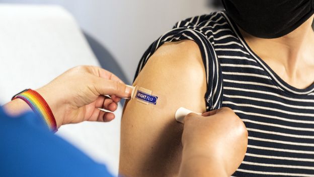 Medical researcher in laboratory examining flu vaccine samples under scientific equipment