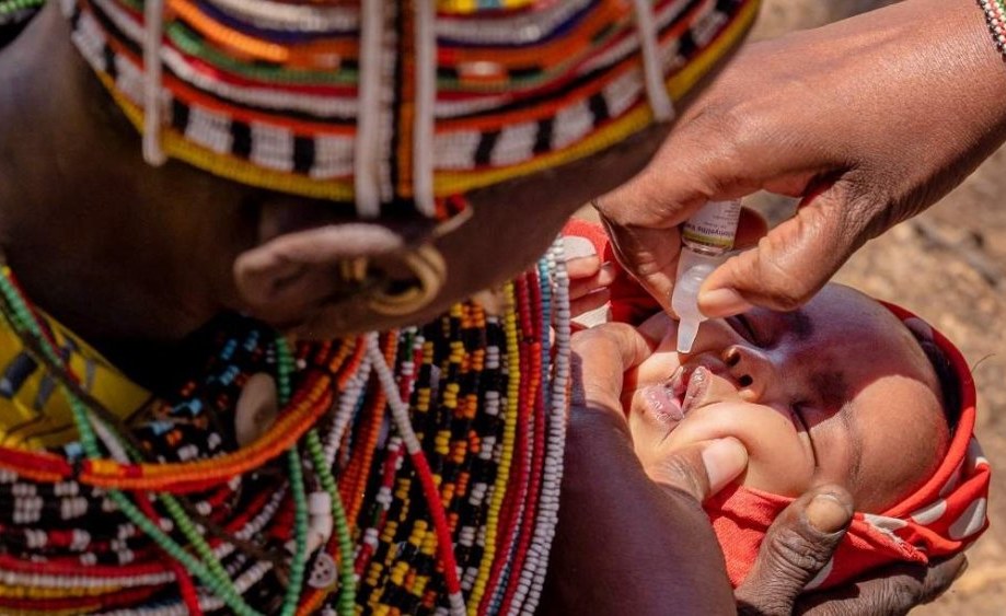 African healthcare worker administering vaccine to smiling child while mother watches nearby