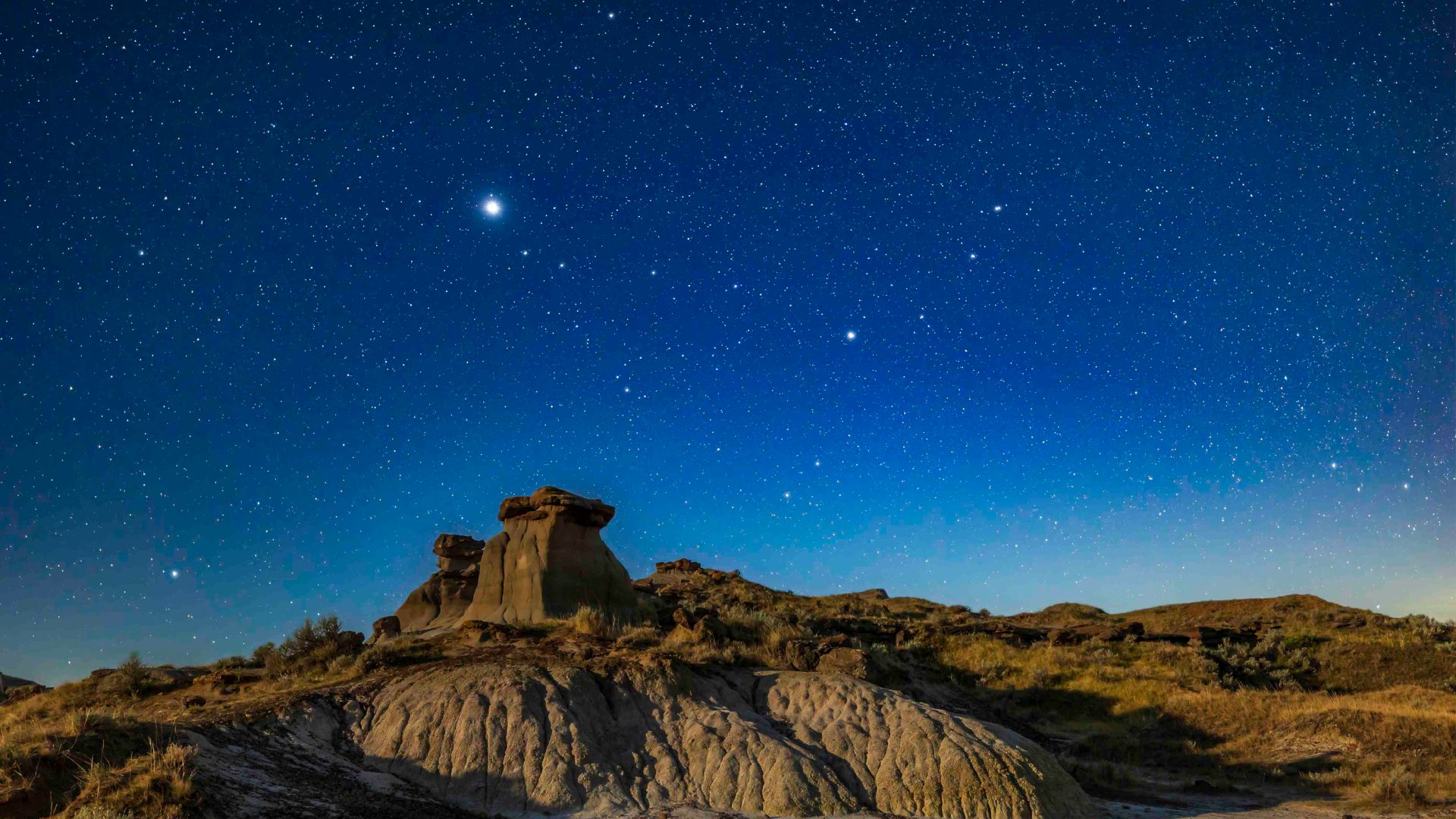 Jupiter and Saturn shining brightly above dark landscape formations under moonless night sky