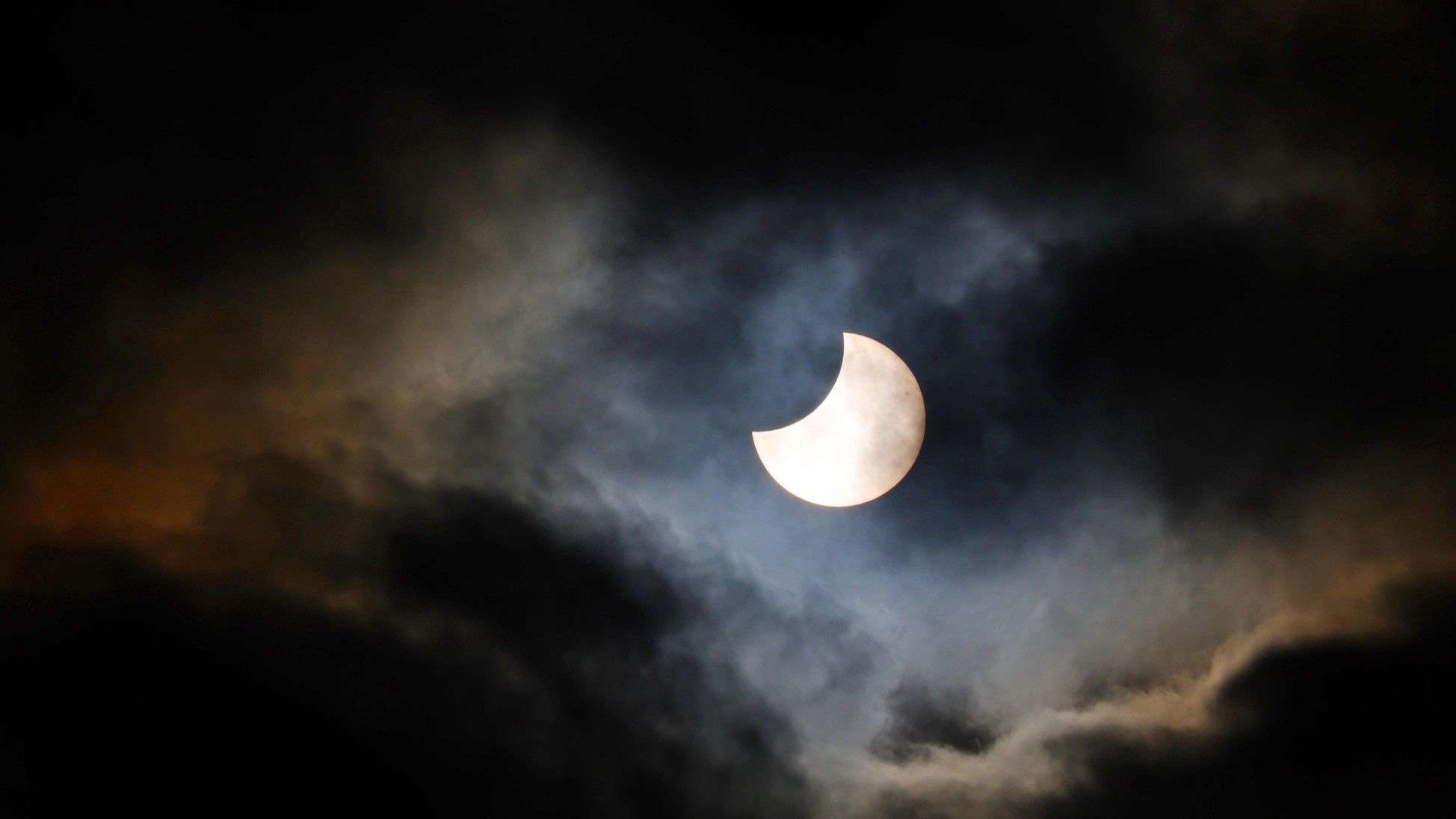 Partial solar eclipse showing moon covering portion of sun in clear blue sky