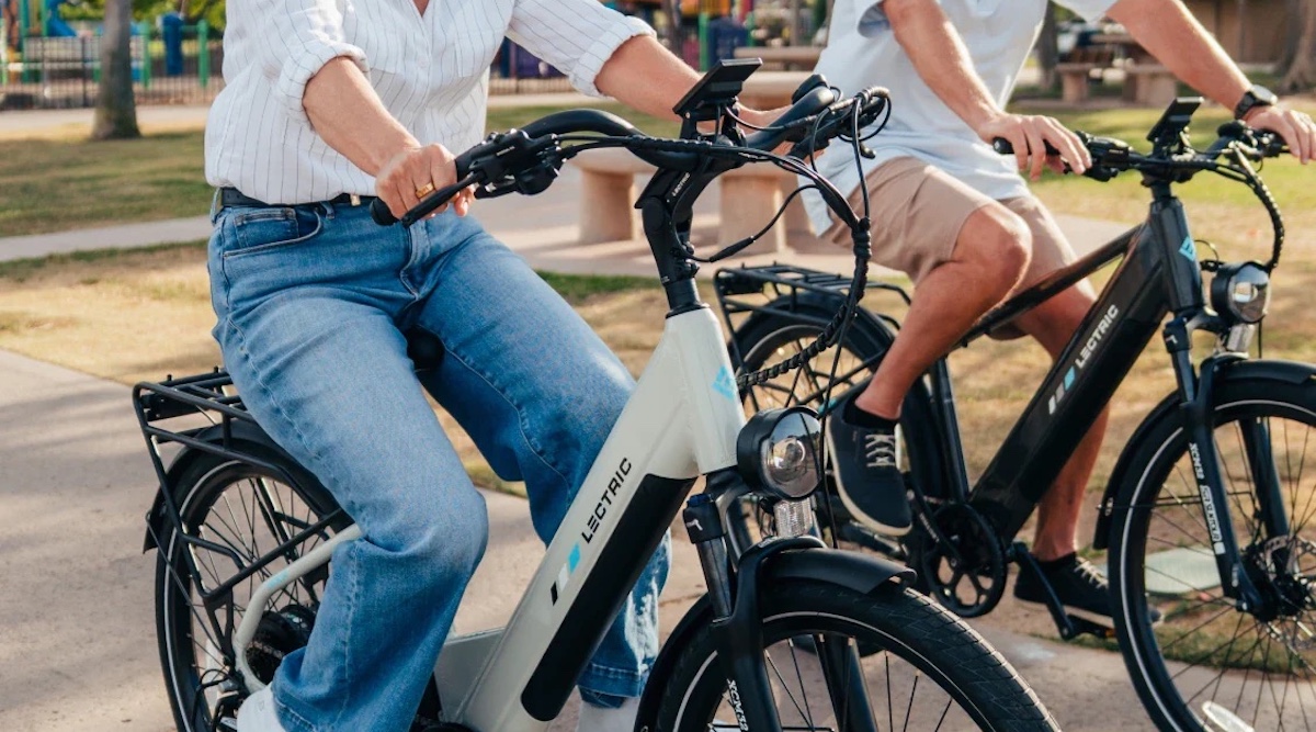 Person smiling while riding electric bicycle on sunny bike path outdoors