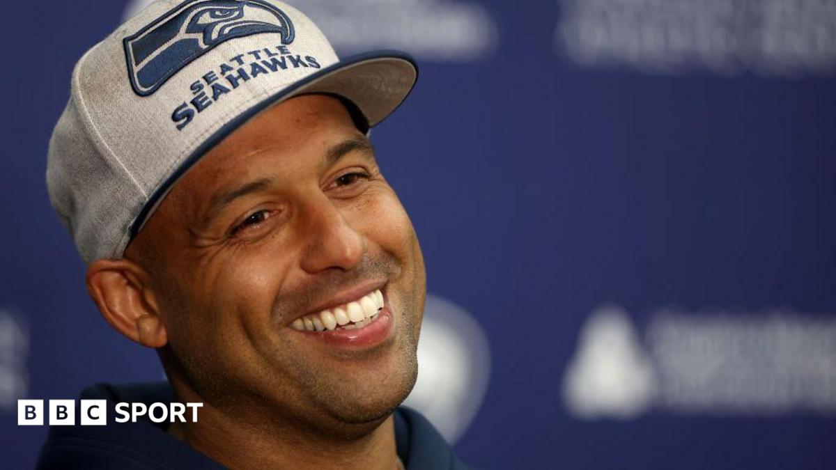 Aden Durde in Seattle Seahawks coaching gear on sideline during NFL game