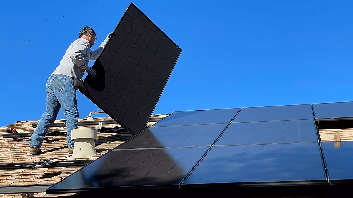 Modern home with dark blue solar panels installed across entire roof under bright sunny sky
