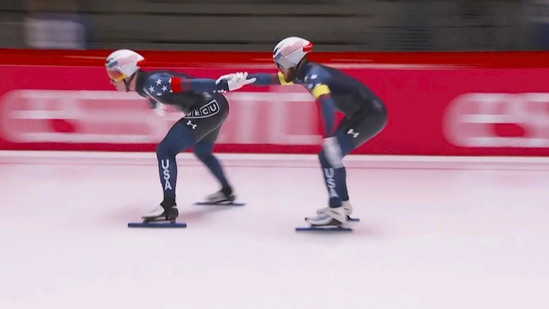 Three American speed skaters racing in team formation on indoor ice track at World Cup