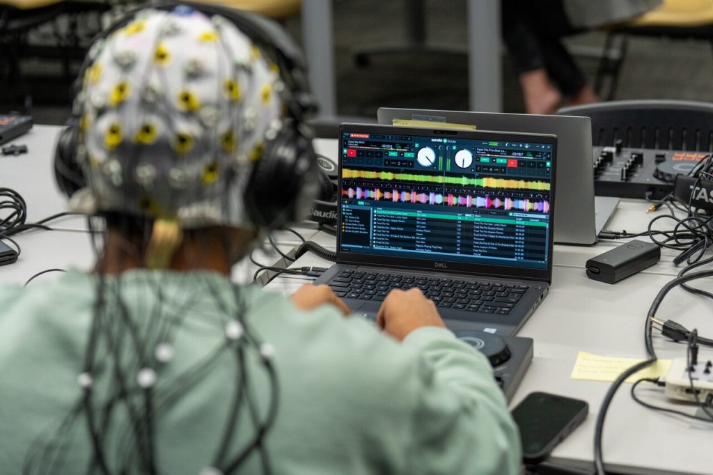 College student wearing EEG cap while mixing music on digital DJ controller during research study