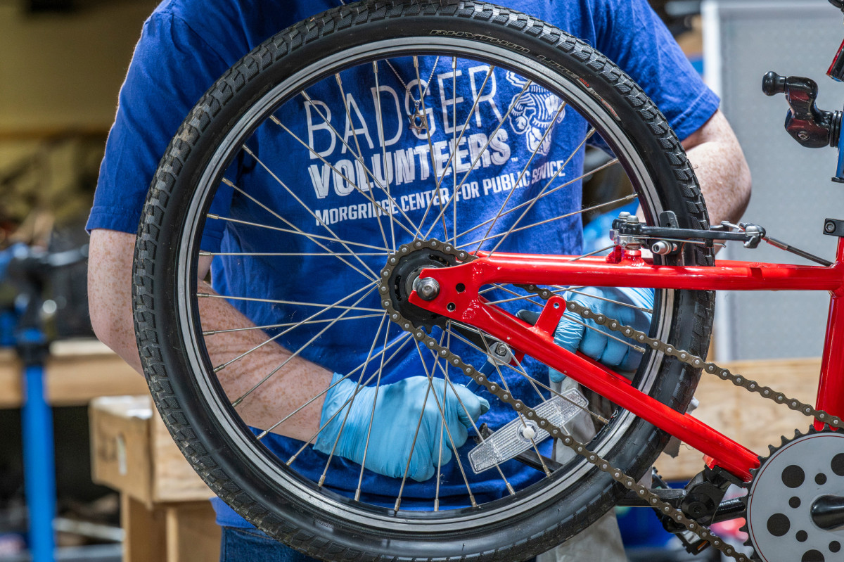 College student in workshop repairing bicycle wheel for donation to child in need
