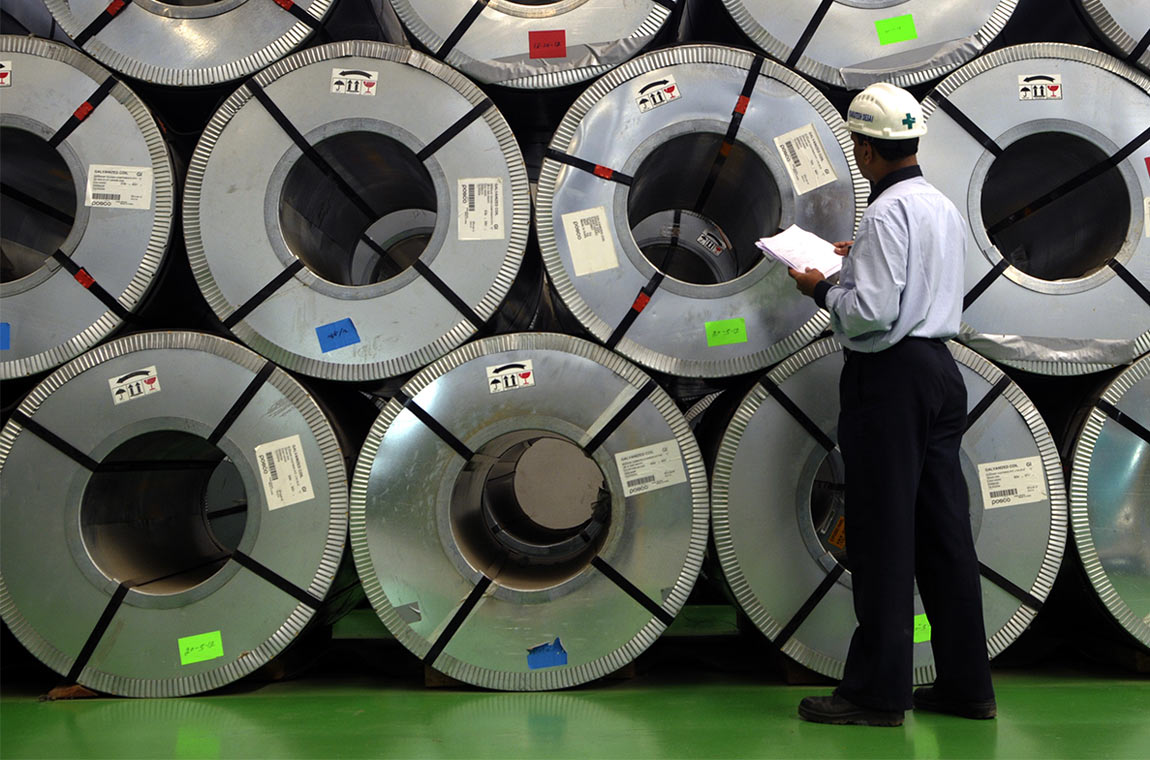 ** Modern steel manufacturing facility with wind turbines visible in background representing green energy transition