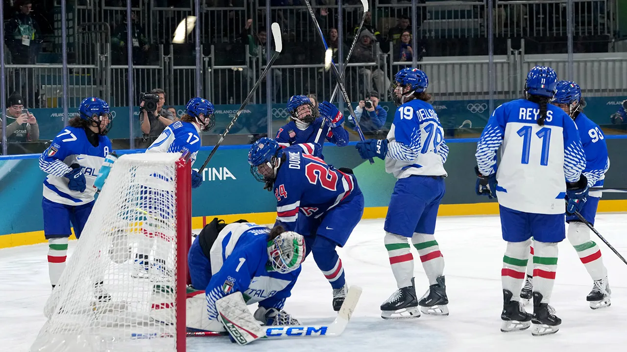 Team USA women's hockey players celebrating together on ice after scoring Olympic quarterfinal goal
