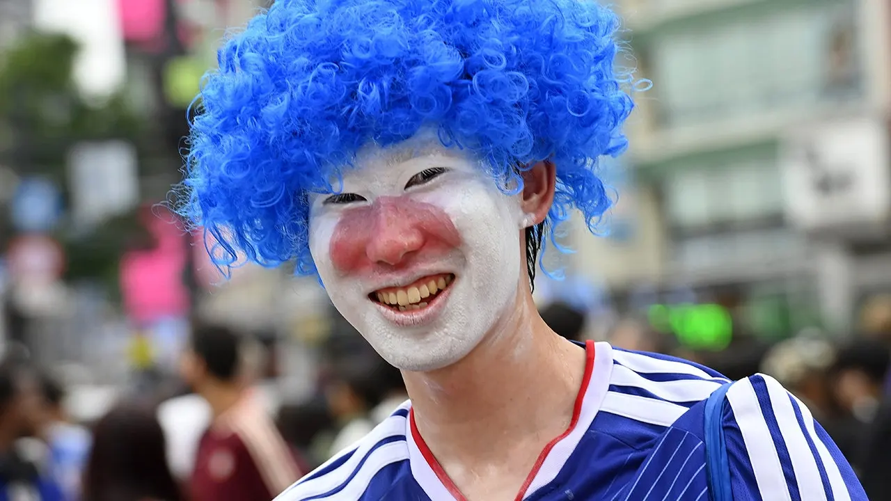 Japanese soccer fan wearing bright blue wig celebrates with Brazilian supporters at World Cup