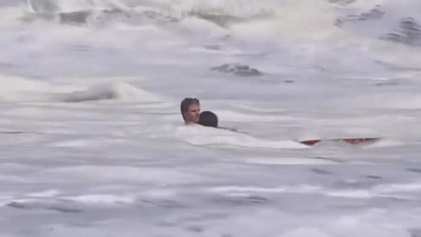 Teenage lifeguard carrying rescued child through powerful crashing waves at California beach