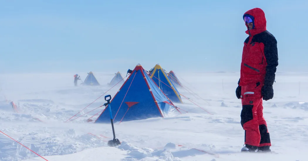 Scientists in winter gear setting up equipment on snowy Antarctic glacier landscape