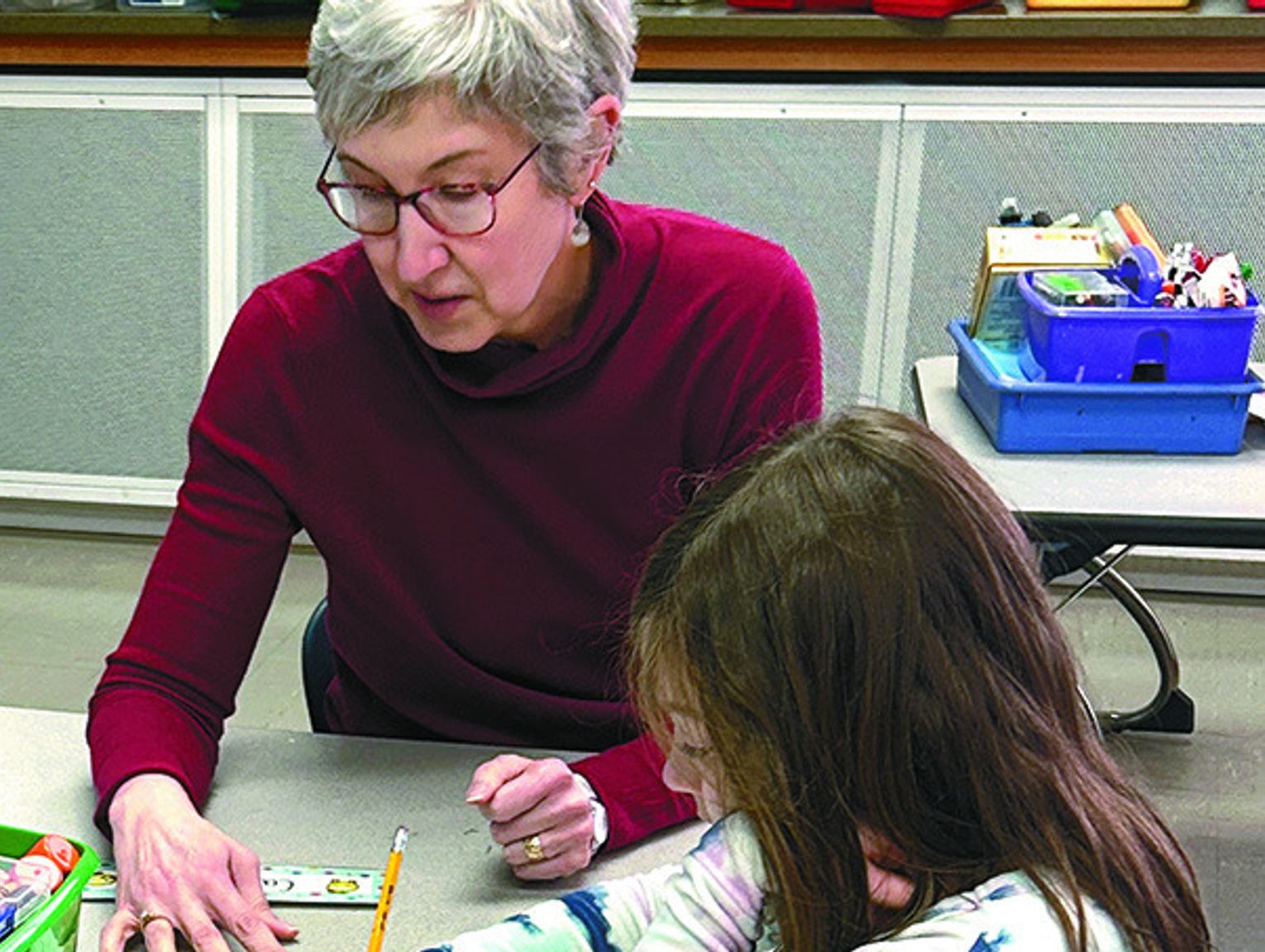 Volunteer tutor working with elementary student on reading assignment at school desk