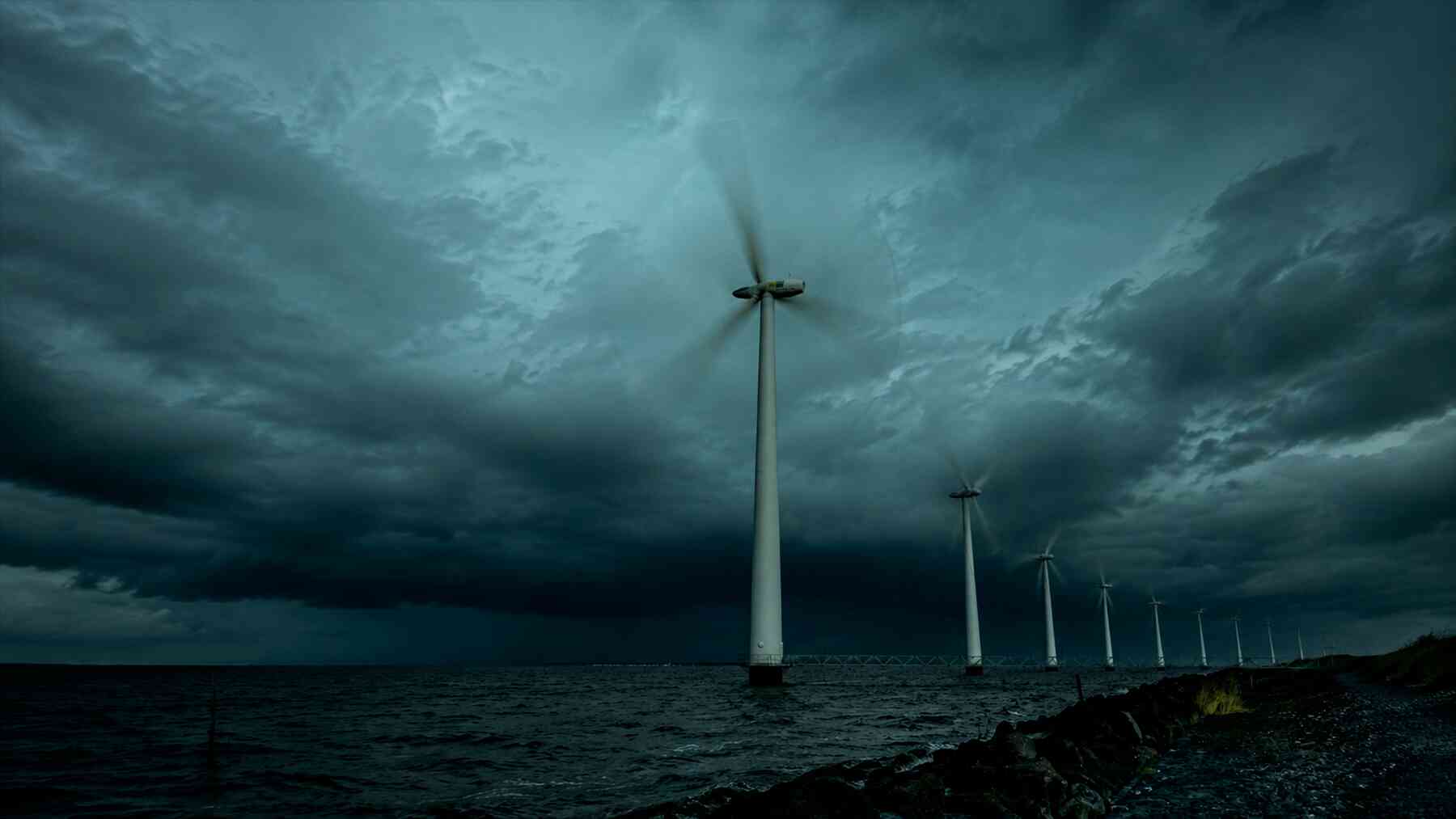 Offshore wind turbines spinning in ocean waters under clear sky creating atmospheric wake patterns