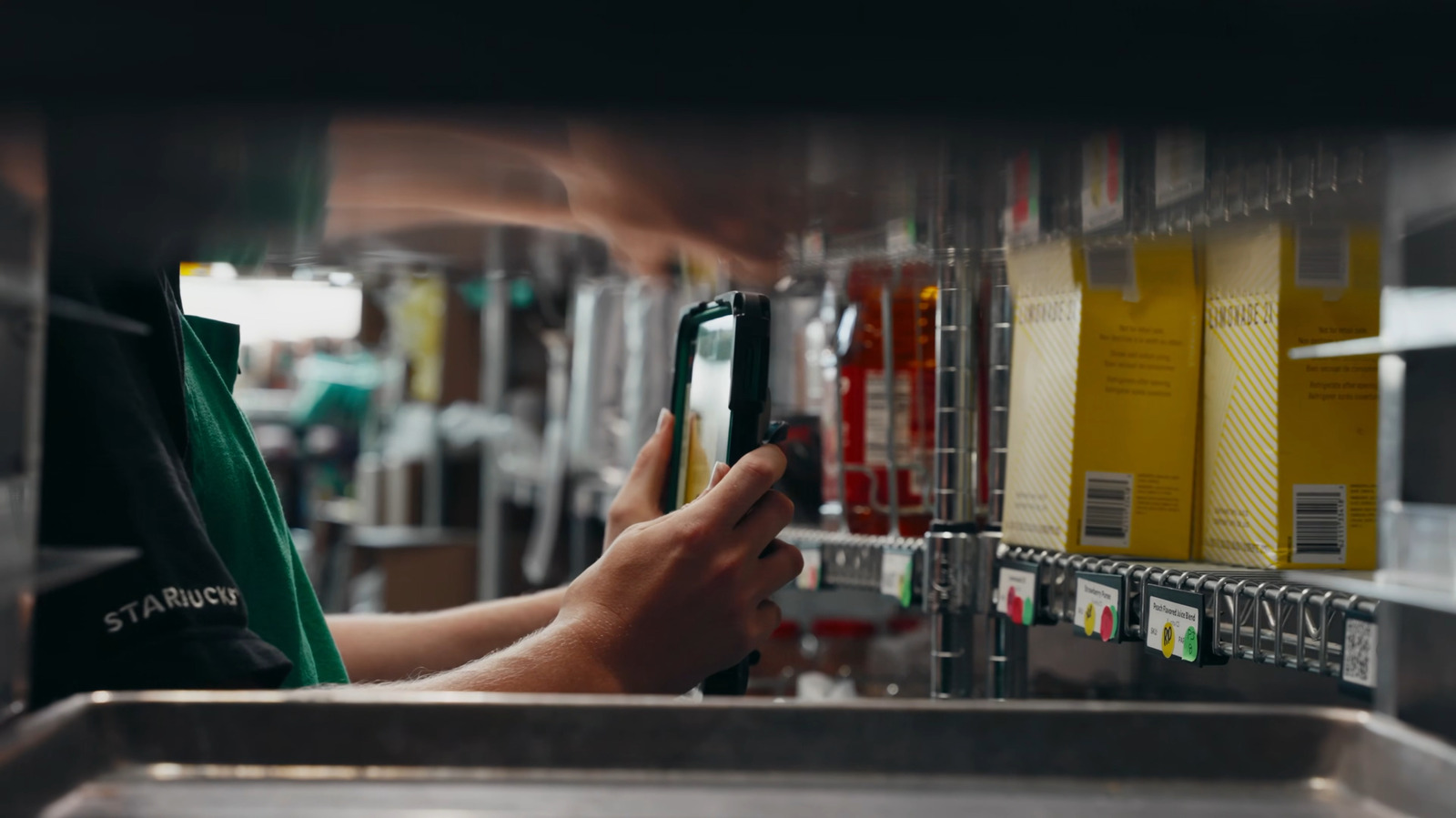 Starbucks barista scanning inventory shelves with handheld device in coffee shop backroom