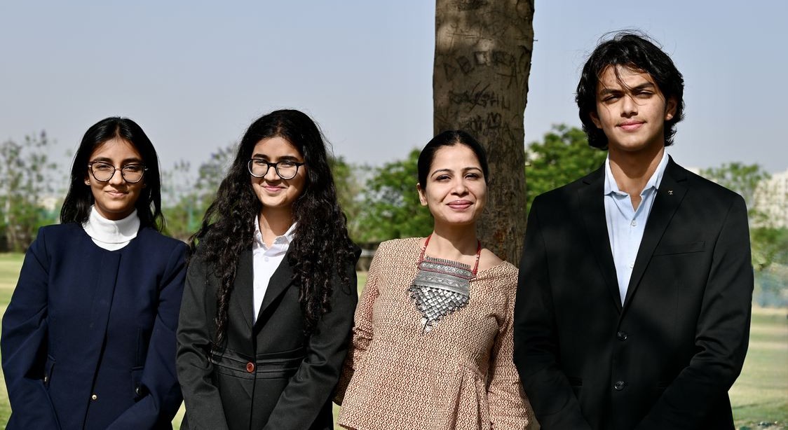 Three Indian teenage students holding their Plas-Stick invention with their teacher at award ceremony