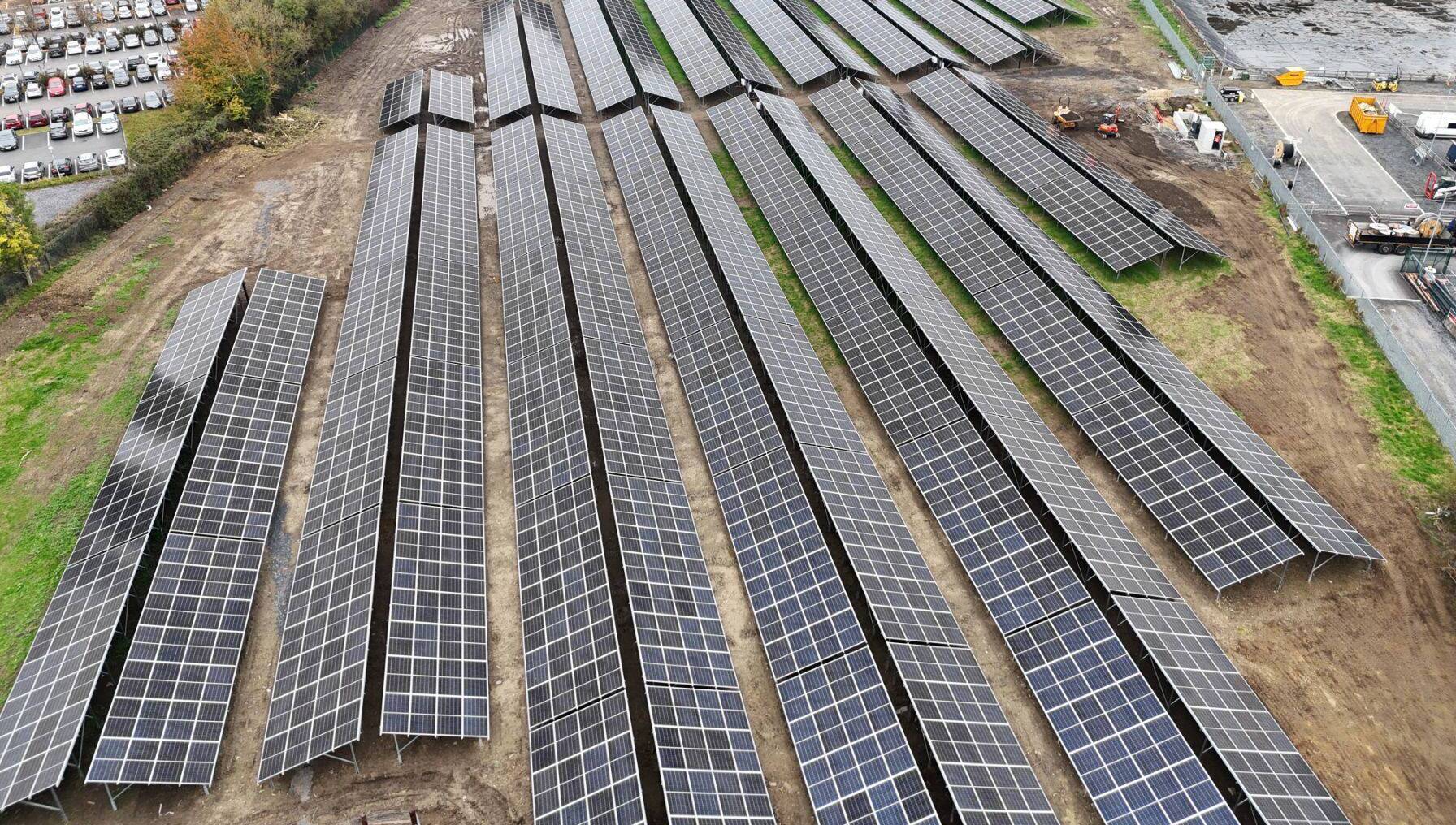 Rows of ground-mounted solar panels stretching across green Irish farmland under sunny skies