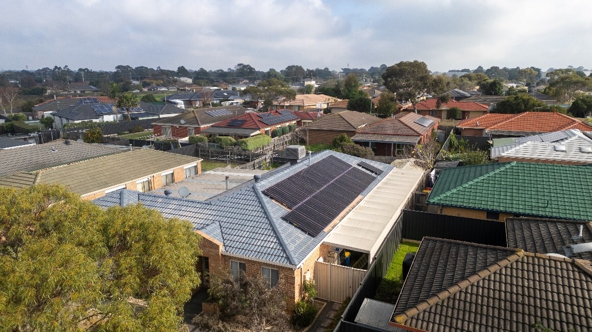 Aerial view of residential neighborhood with solar panels covering rooftops under clear blue sky