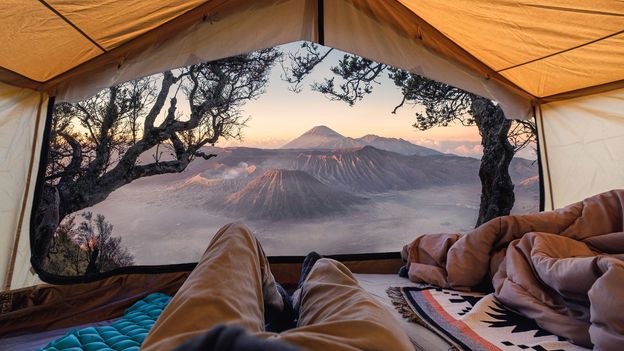 Person sleeping peacefully in sleeping bag inside tent at sunrise with natural light